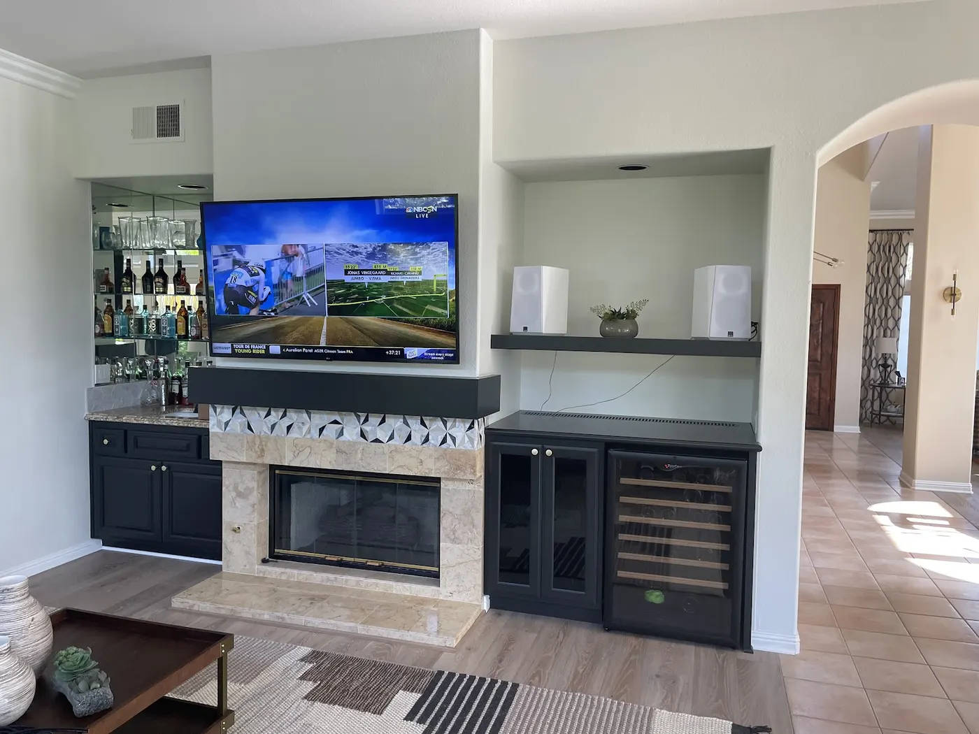 Dark custom cabinetry around a stone fireplace with a TV and a wine fridge