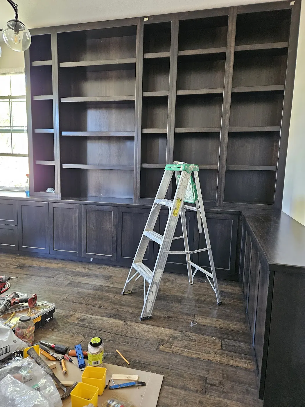 Dark built in bookcases mid install, a ladder and tools on the floor