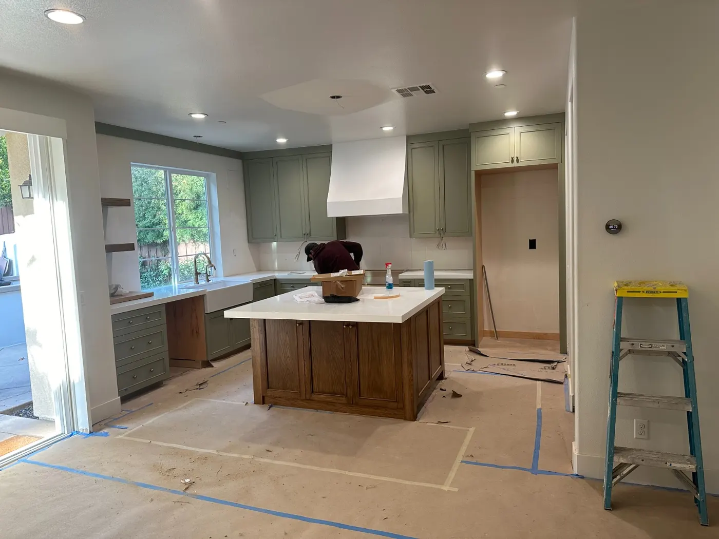 Kitchen mid install with a stained island and new cabinets, floors still covered