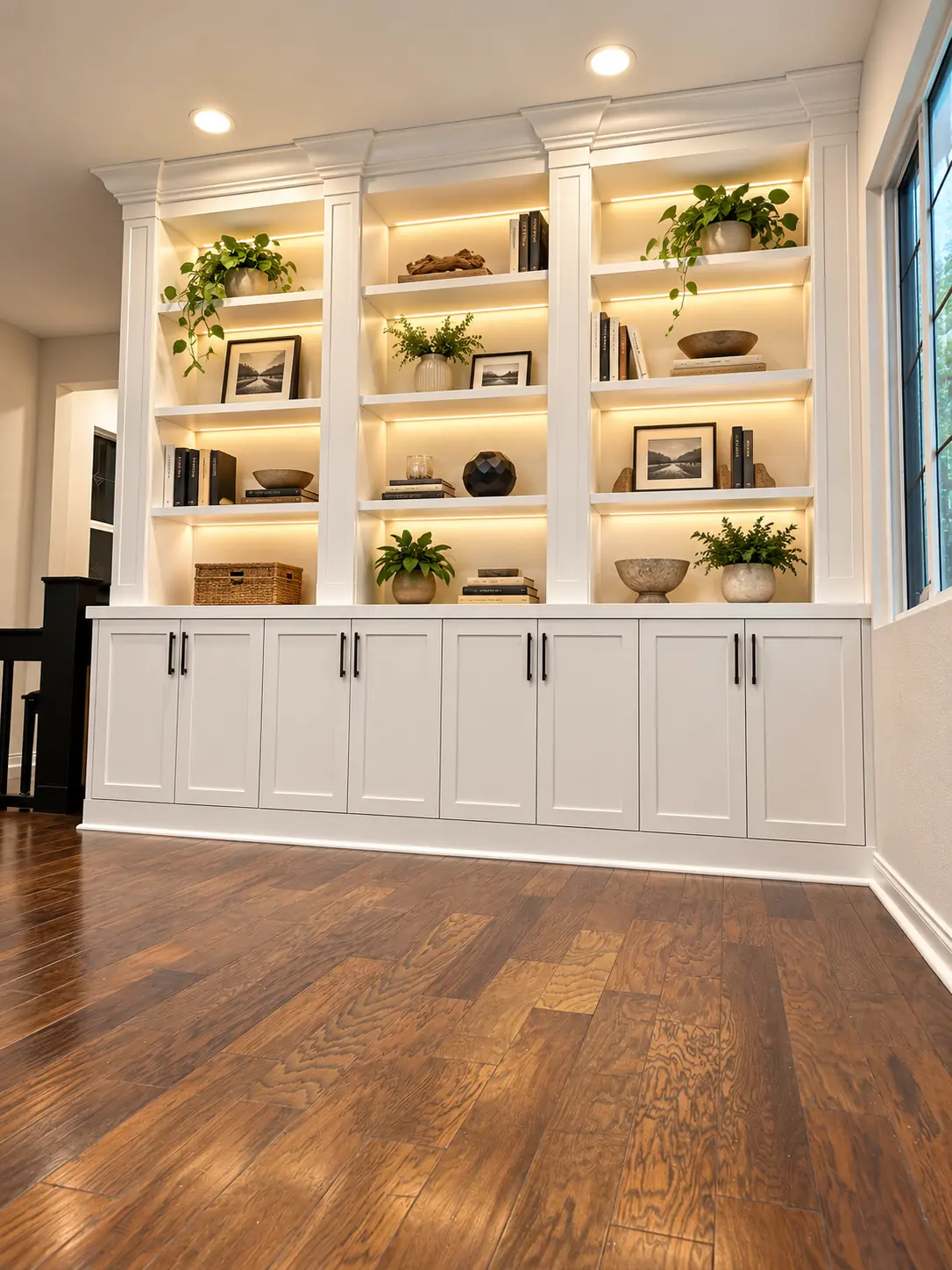 White built in bookcases with lit shelves above paneled cabinets