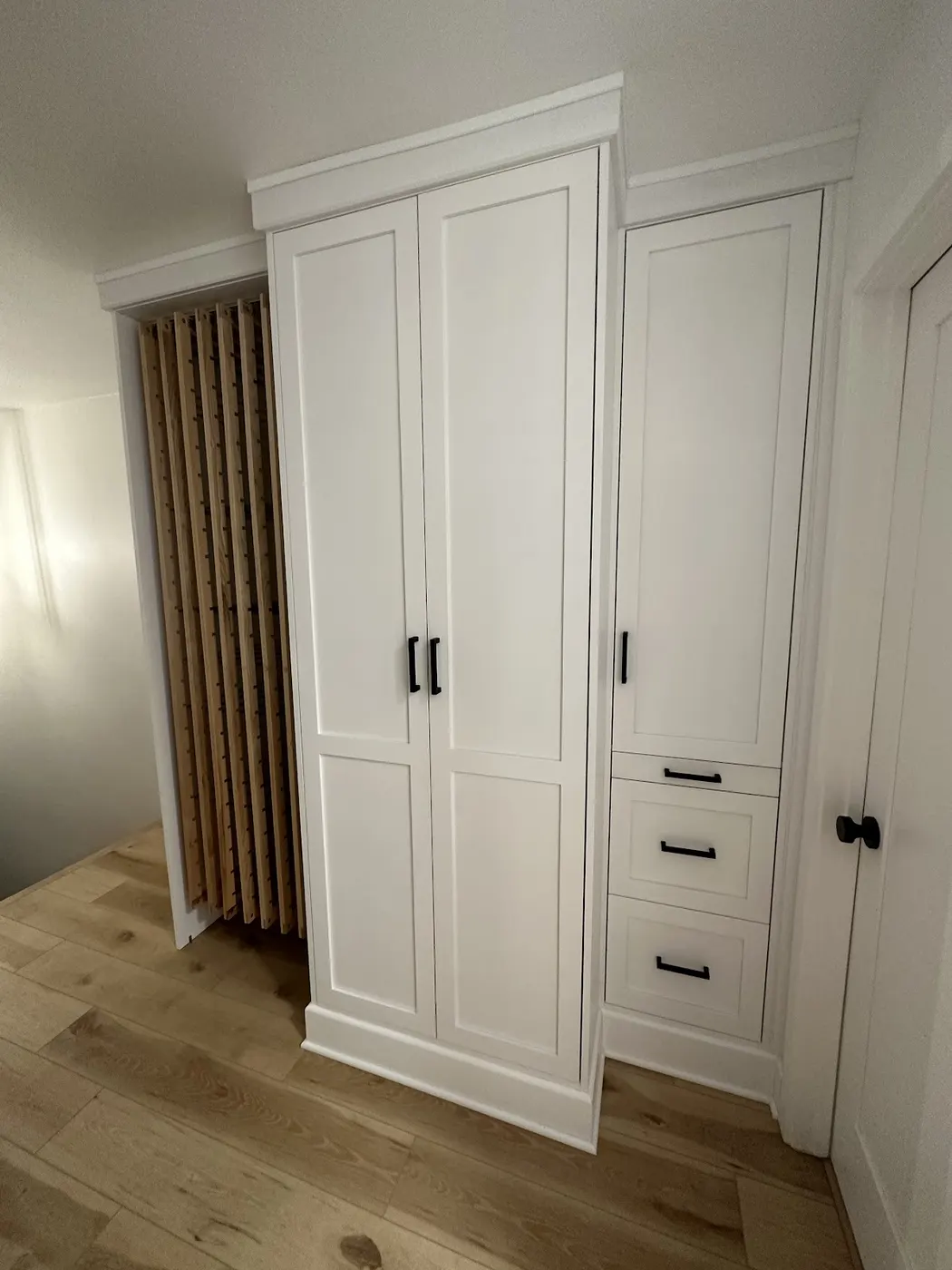 White laundry machine cabinetry with an oak slat dryer rack beside it