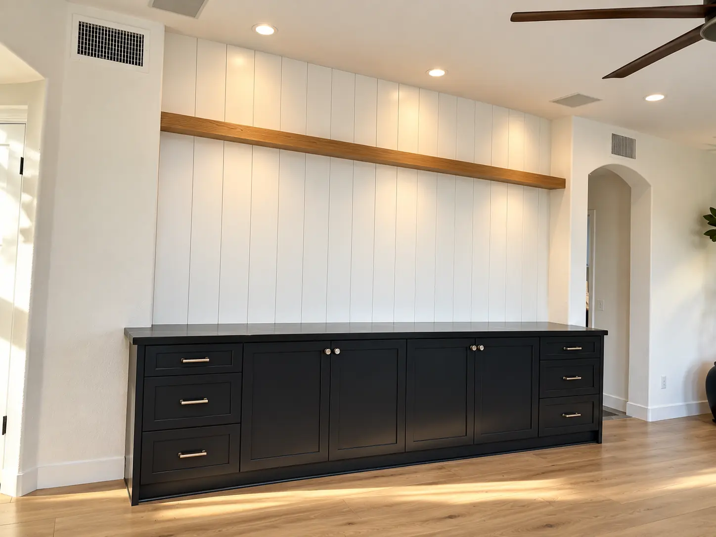 Black console cabinet below a white paneled wall with an oak shelf